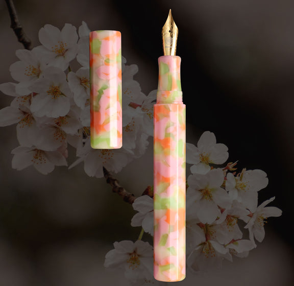 カレイド万年筆・ピンク・和桜、桜を背景に淡いピンクとグリーンのマーブル軸を見せた全体カット - Wancher ワンチャー